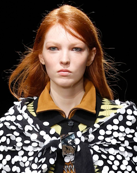 A model with red slideparted hair wearing a collared shirt and a sequined cape